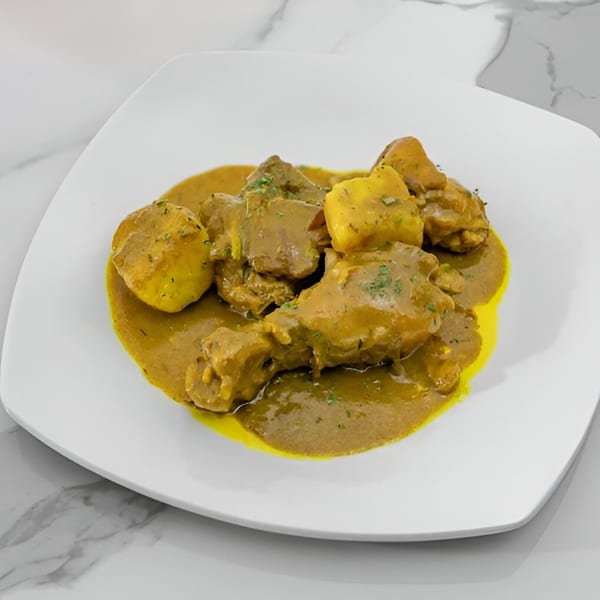 Curried chicken and potatoes in a rich yellow sauce, garnished with herbs, on a white plate.