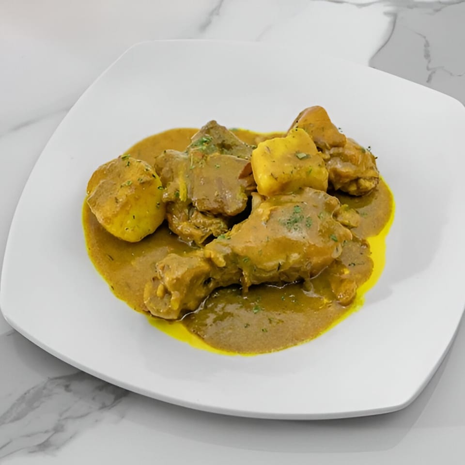 Curried chicken and potatoes in a rich yellow sauce, garnished with herbs, on a white plate.