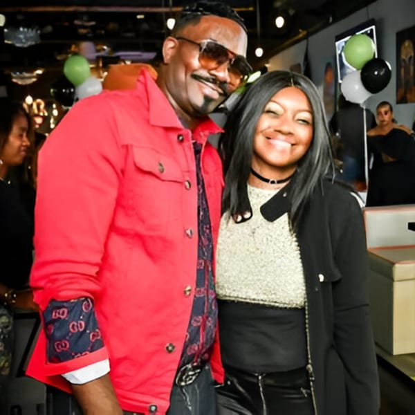A man in a red jacket and sunglasses with a woman in a black jacket smiling at Jewlz Bar.