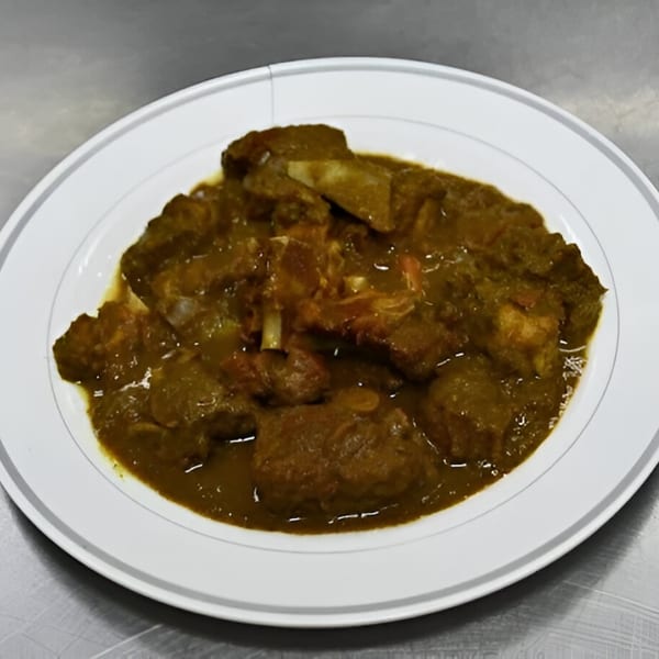 A white plate filled with a rich, dark green Jamaican curry with chunks of meat and bones.