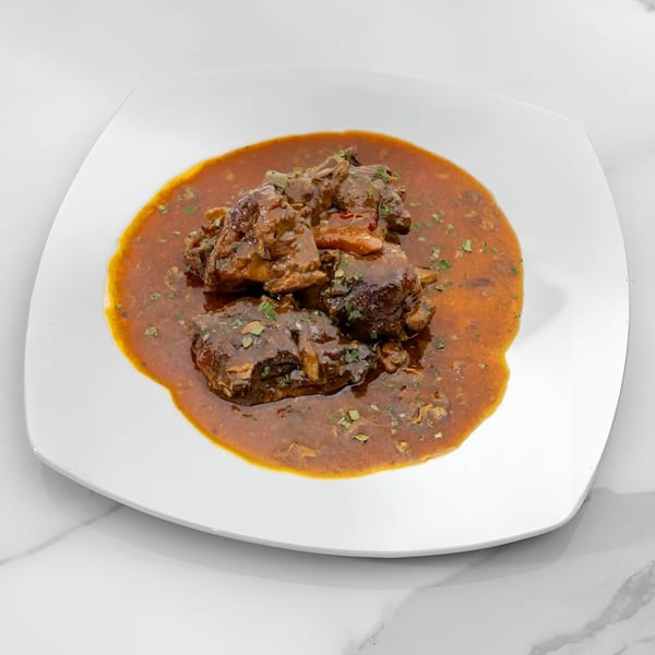 Jewlz Bar's Jamaican oxtail stew, rich brown meat in a savory sauce, garnished with herbs.