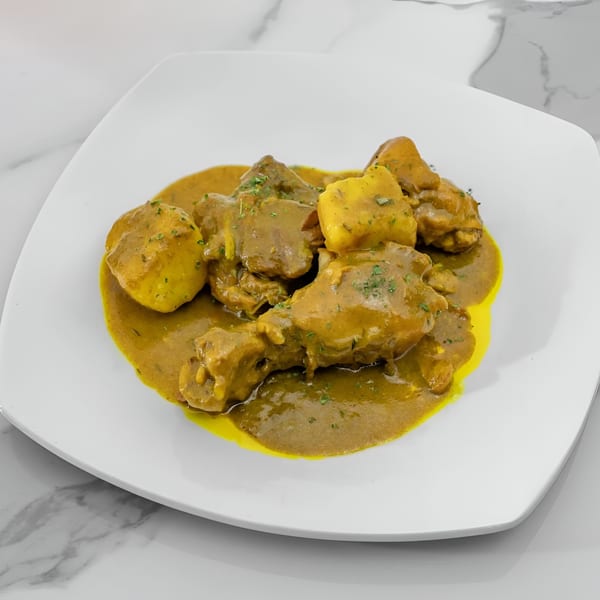 Curried chicken and potatoes in a rich yellow sauce, garnished with herbs on a white plate.