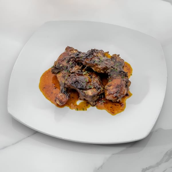 Jamaican jerk chicken pieces with a rich, dark sauce and green herbs on a white plate.
