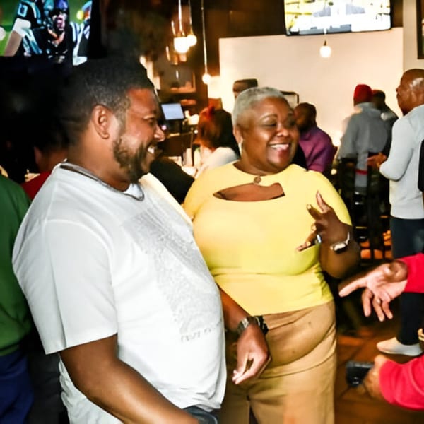 Smiling man and woman enjoying themselves at Jewlz Bar, with a football game on TV in the background.