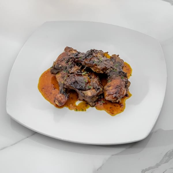 Jamaican jerk chicken pieces with a rich, orange sauce on a white square plate.