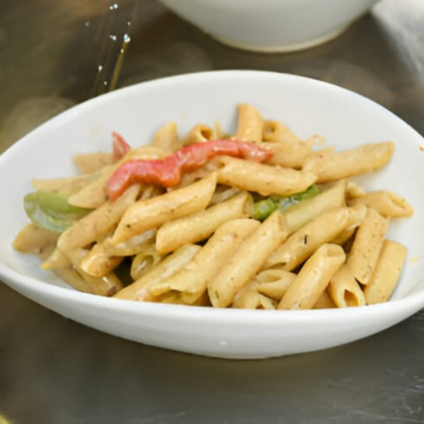 A white bowl filled with Jamaican-style penne pasta, red and green bell peppers, and a creamy sauce.